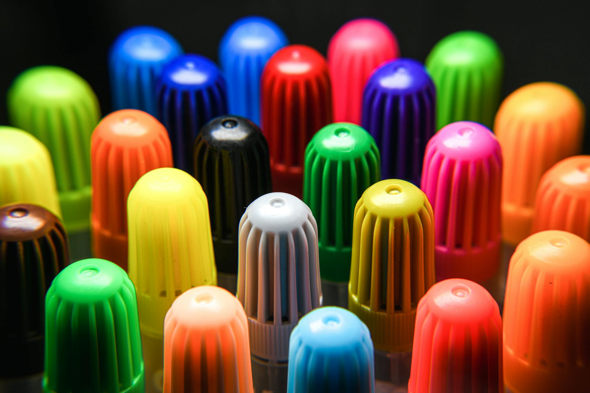 Vibrant close-up of colored marker caps arranged in rows against a dark backdrop.